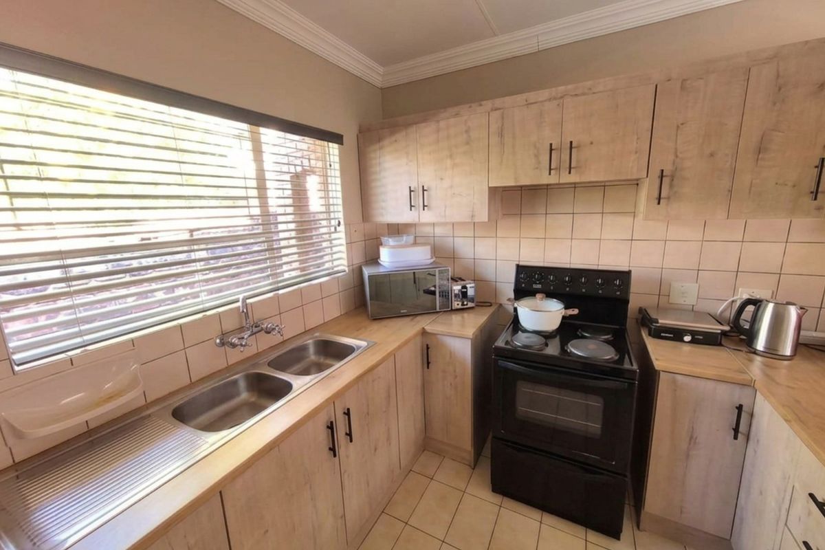 Functional kitchen featuring light wood-look cabinetry, tiled splashbacks, a double stainless steel sink, and a freestanding electric stove with oven.