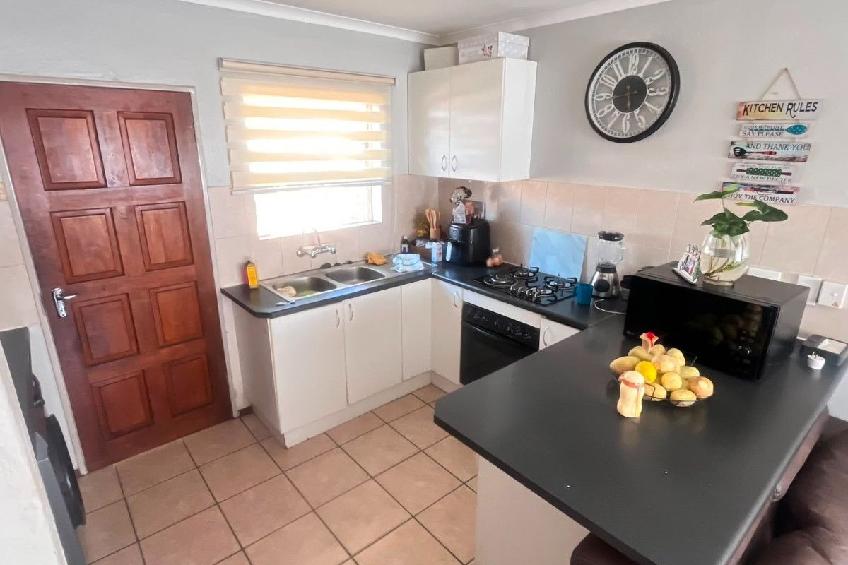 A functional kitchen featuring white cabinetry, dark laminate countertops, a gas hob, built-in oven, and tiled flooring with a double basin sink.