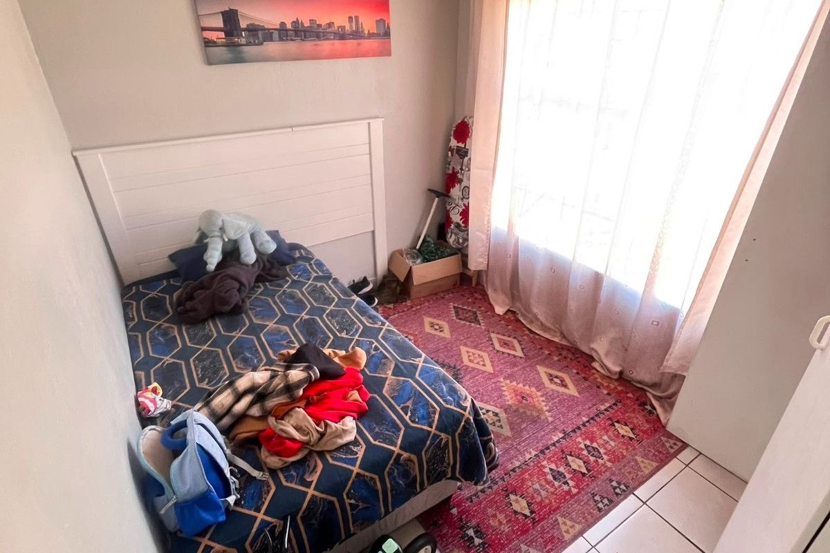 A compact bedroom featuring tiled flooring and a built-in headboard, offering a functional space with natural light from the window.