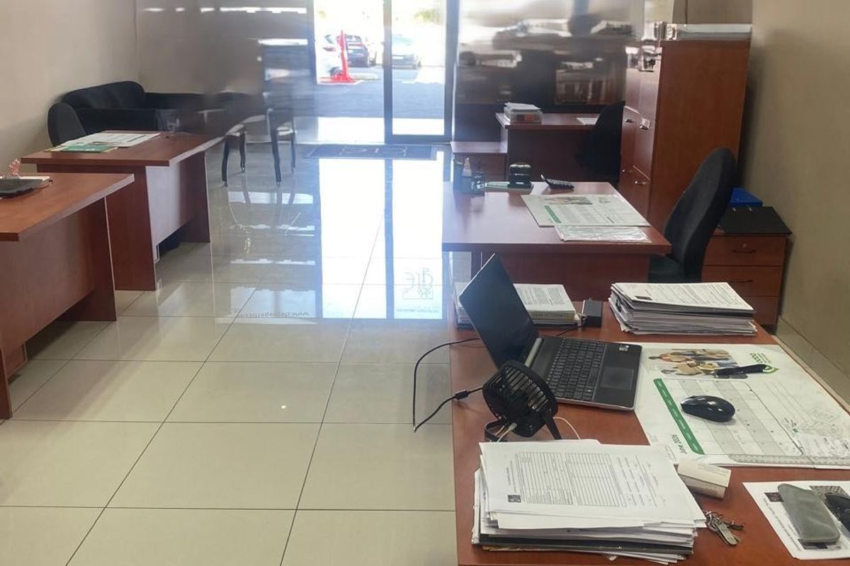 A functional office space featuring polished tiled flooring, a drop ceiling with recessed lighting, and a glass entrance door providing natural light.