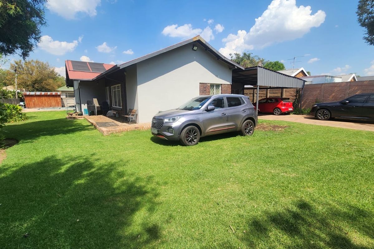 Rear view of the house featuring a metal roof with solar panels, a carport, and a spacious lawn area.
