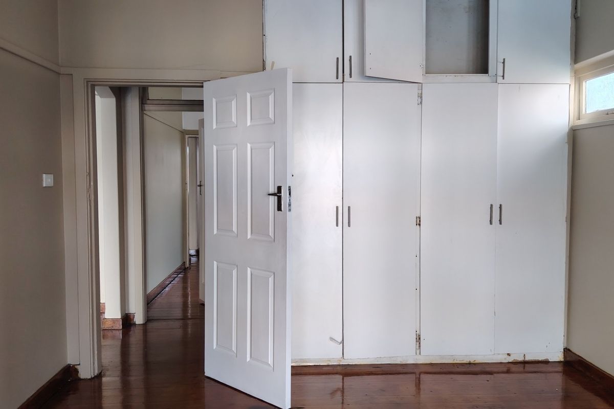 An empty bedroom featuring original hardwood flooring and extensive built-in cupboard storage, requiring minor cosmetic updates to restore its appeal.