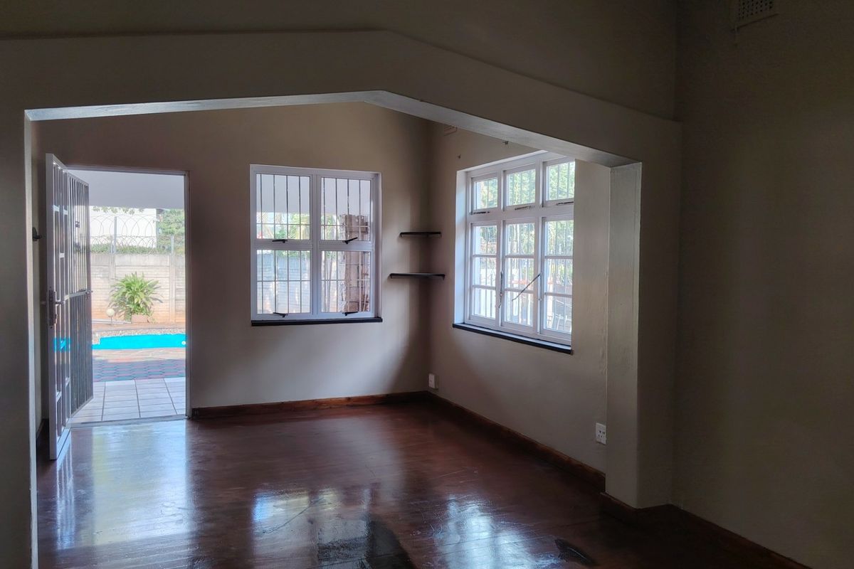 An empty living room featuring polished wooden floors, an architectural archway, and direct access to an outdoor patio area with a pool.