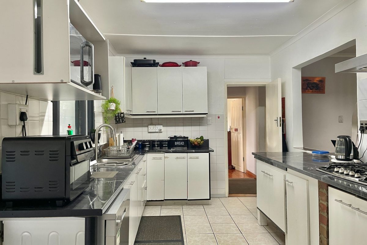A functional kitchen featuring white built-in cabinetry, dark laminate countertops, a gas hob, and tiled flooring, offering a practical layout for daily meal preparation.