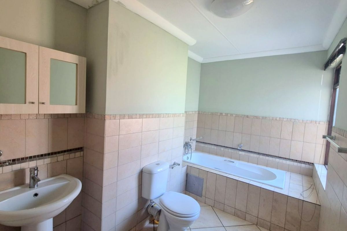 A functional bathroom featuring a built-in bathtub, pedestal sink, and toilet, finished with neutral wall tiles and flooring.