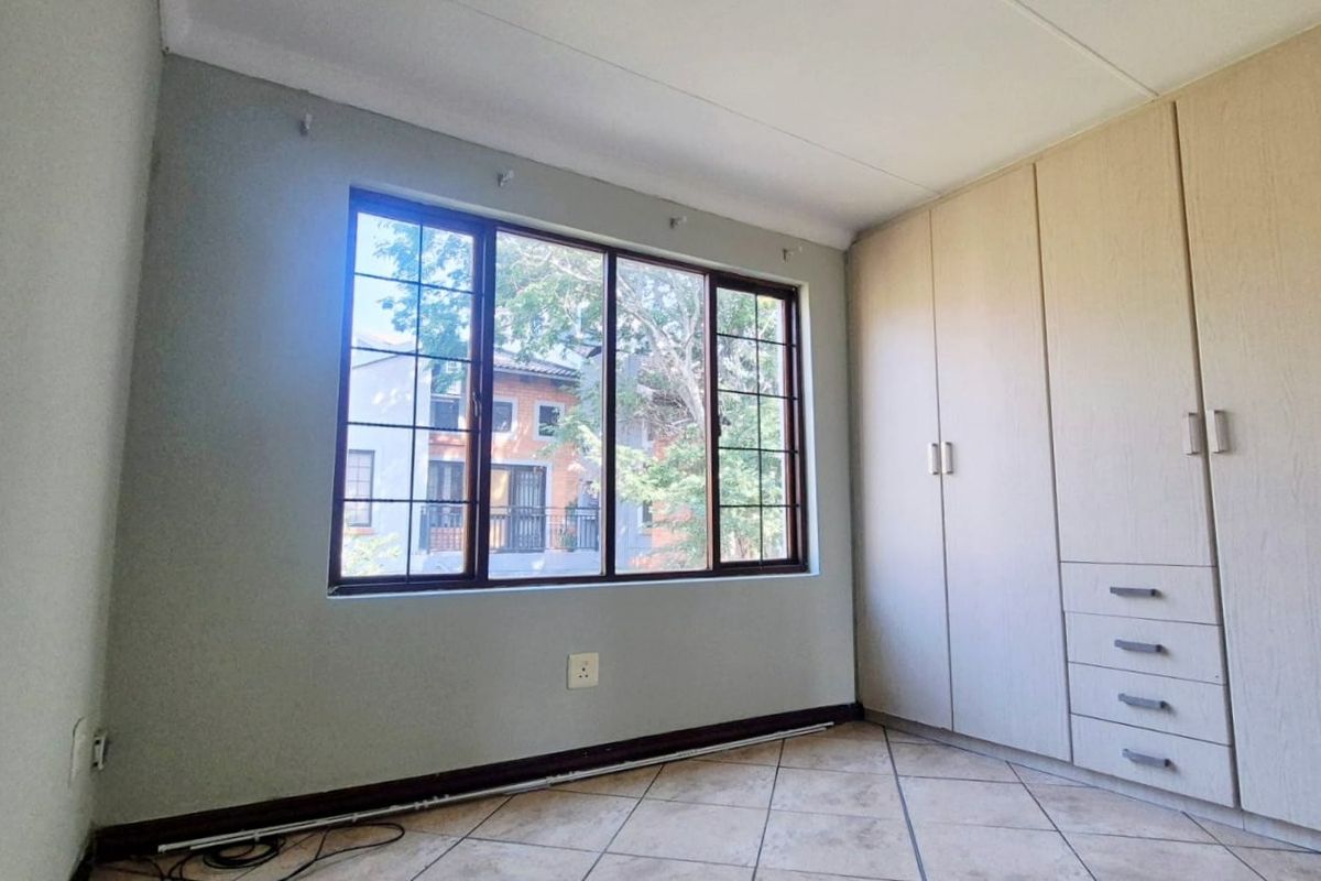A bright, empty bedroom featuring neutral tiled flooring, built-in wooden cupboards, and a large window providing natural light.
