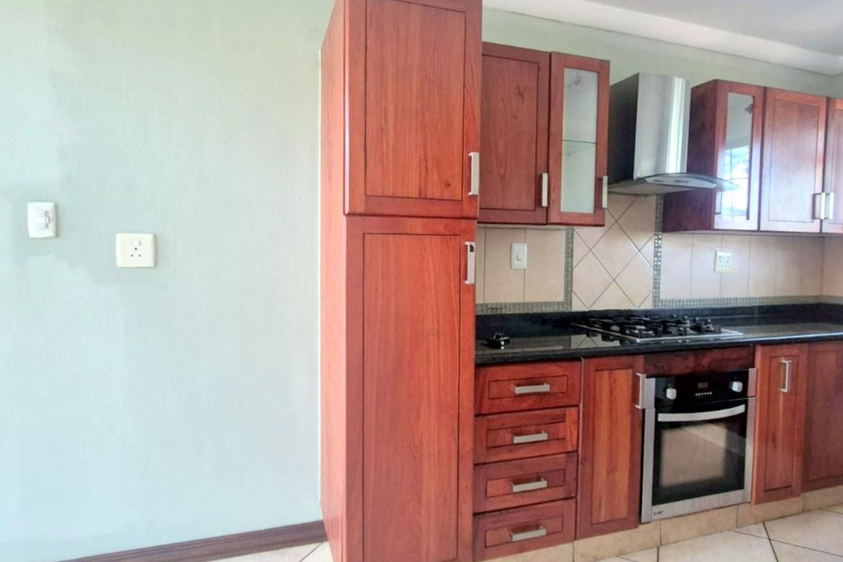 A functional kitchen featuring warm-toned wooden cabinetry, granite countertops, a built-in oven, gas hob, and a stainless steel extractor fan.
