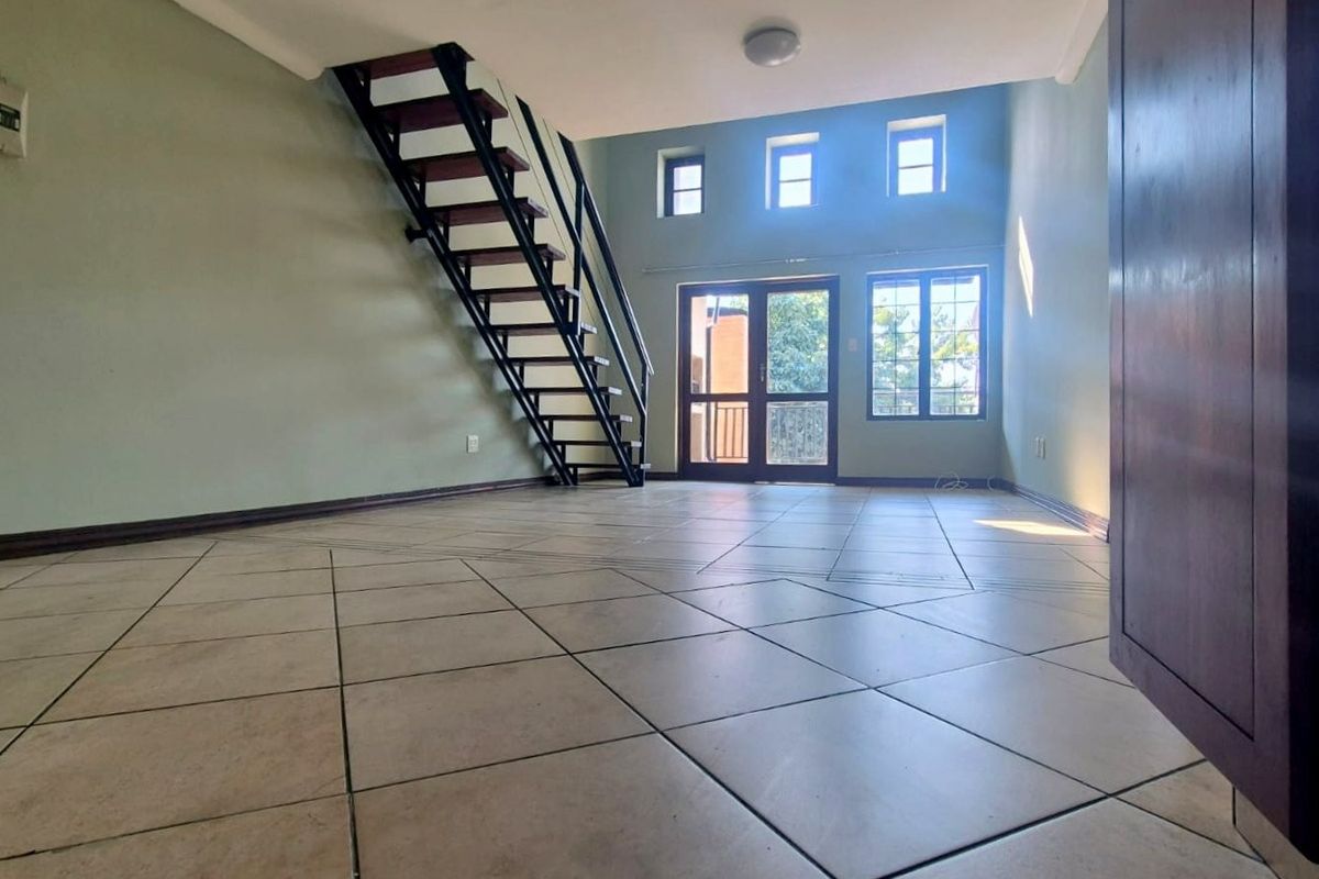 Spacious, empty living area featuring tiled flooring, an open-tread staircase, and large windows providing natural light with access to an outdoor area.