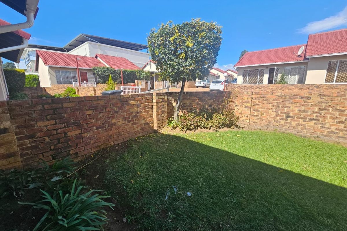 A private rear garden area featuring a well-maintained lawn enclosed by a sturdy brick boundary wall, typical of townhouse living.