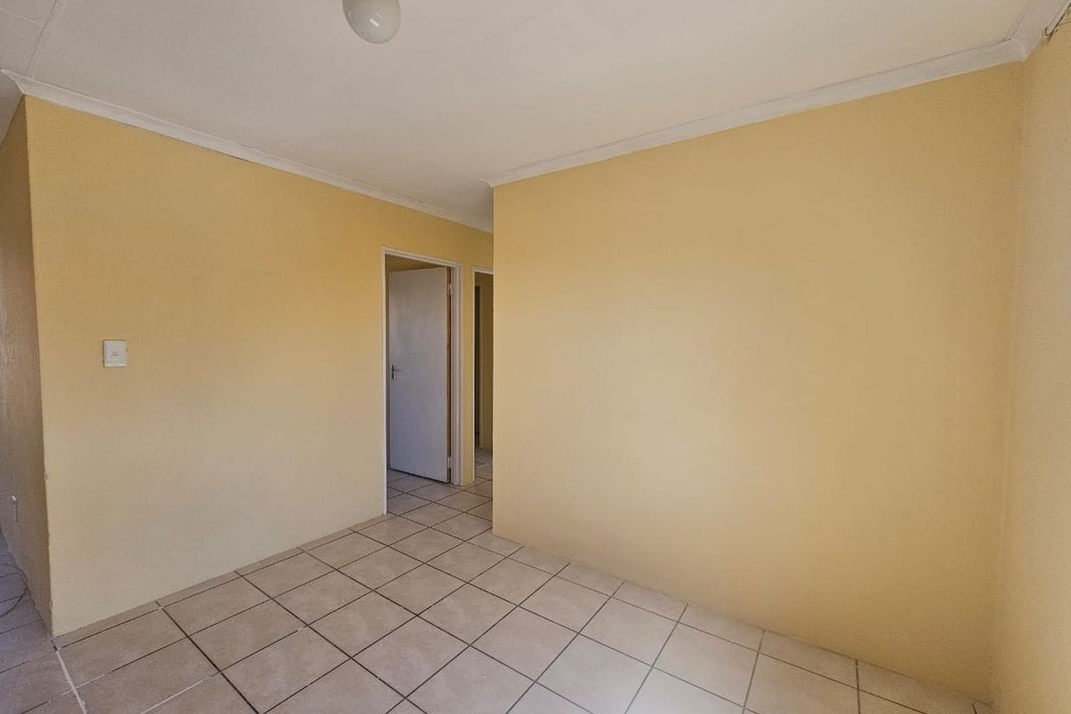 An empty bedroom featuring neutral tiled flooring, coved ceilings, and plain yellow walls, providing a blank canvas for potential renovation or staging.