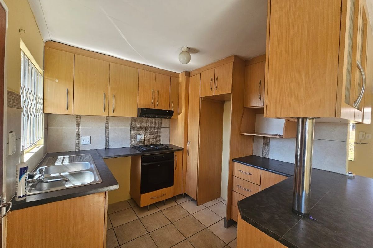 A functional kitchen featuring light wood laminate cabinetry, built-in oven, gas hob, extractor fan, and tiled flooring with ample counter space.