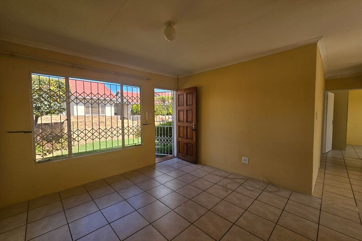 An empty living room featuring tiled flooring, security bars on the windows, and a timber entrance door leading to the exterior.