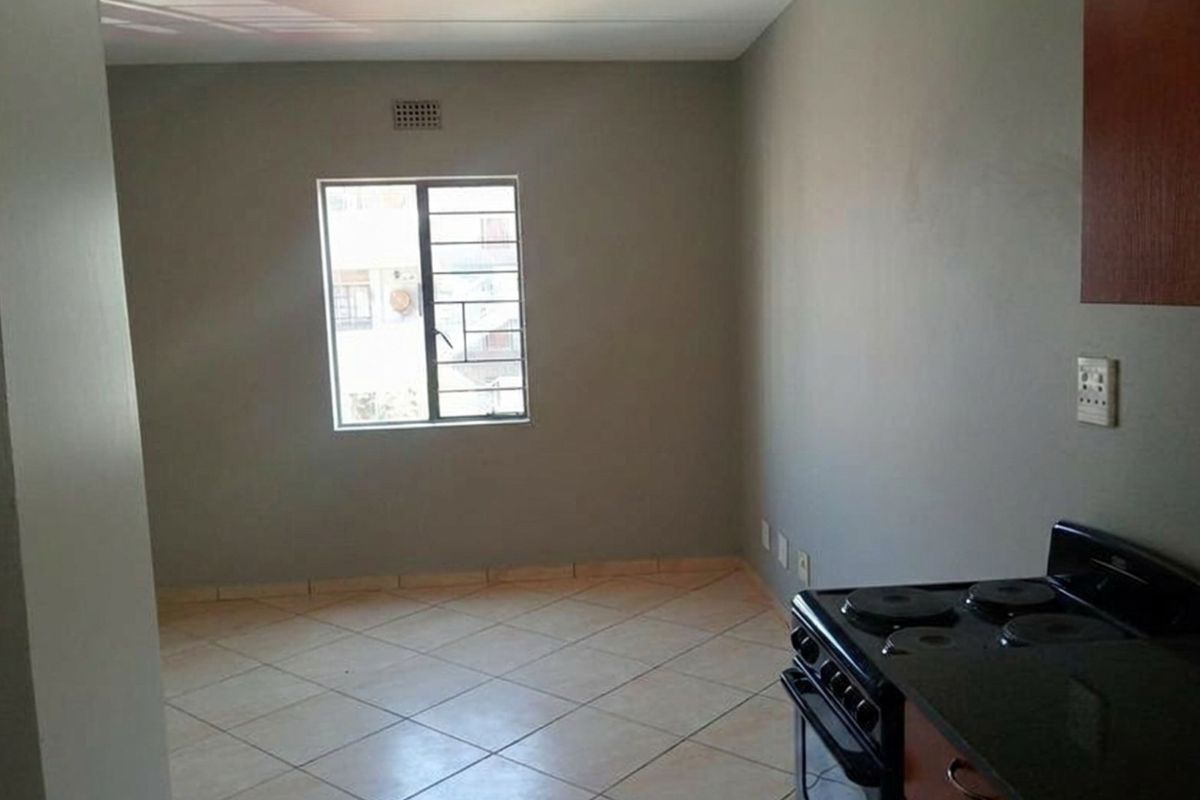 A functional kitchen area featuring tiled flooring, a built-in stove, and a window with security bars.