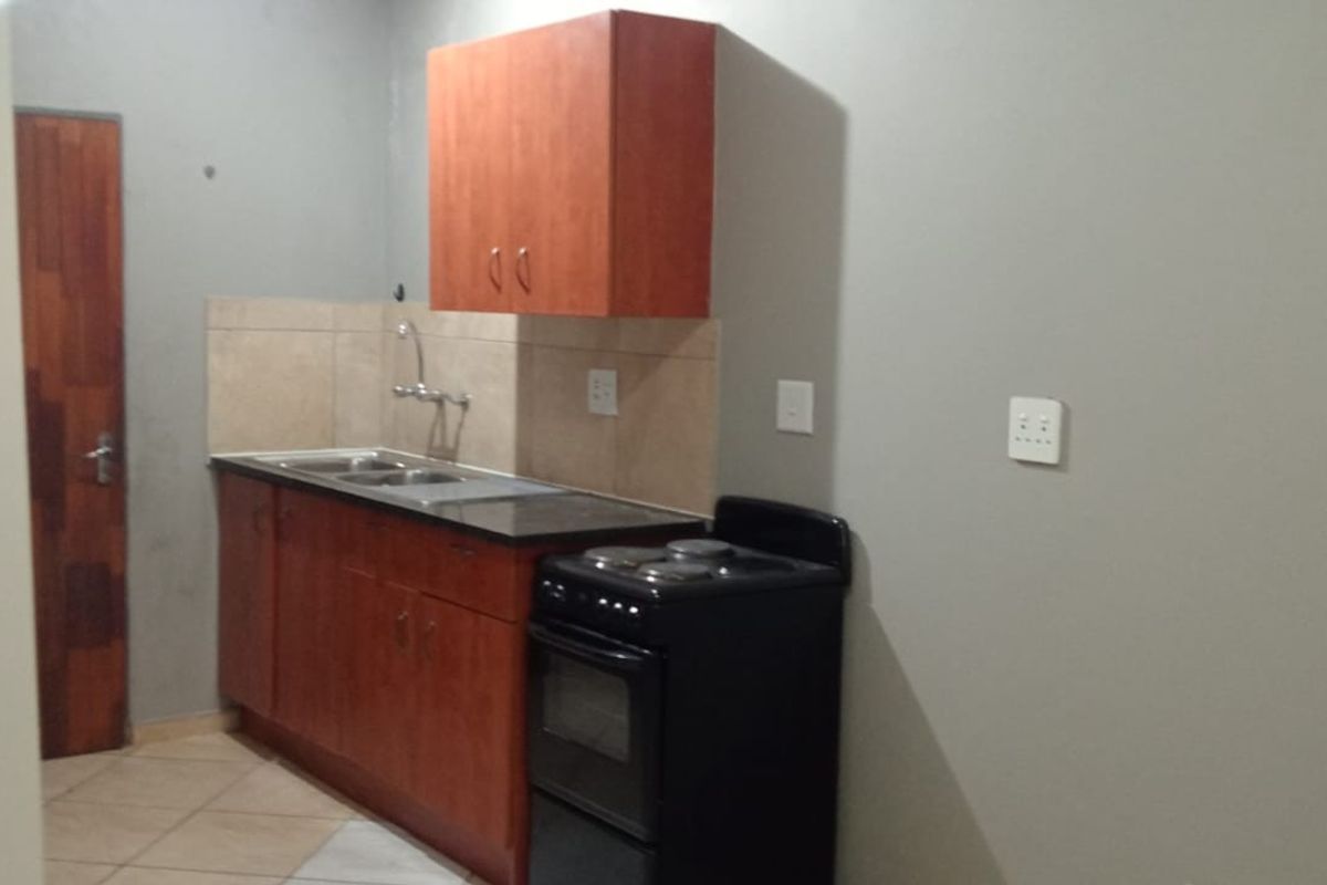 A compact kitchen featuring wooden cabinetry, a stainless steel sink, tiled backsplash, and a freestanding stove, offering a functional layout for a small space.