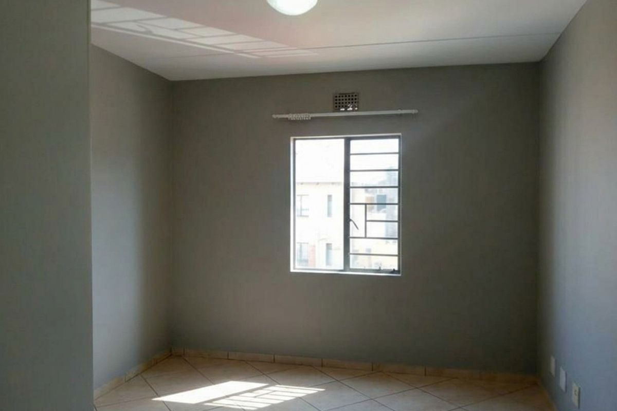 An empty bedroom featuring neutral grey walls, tiled flooring, and a window fitted with security bars.