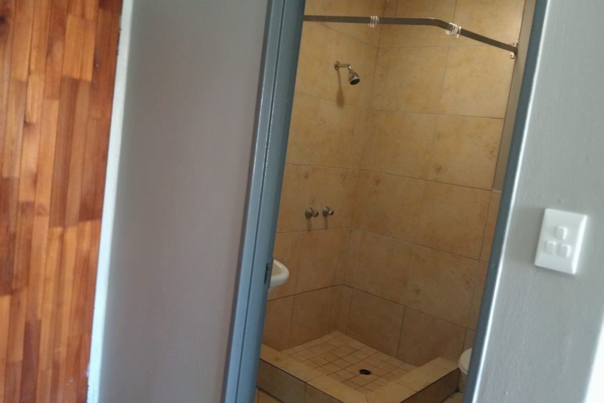 A functional bathroom featuring a tiled shower enclosure with a wall-mounted shower head and mixer.