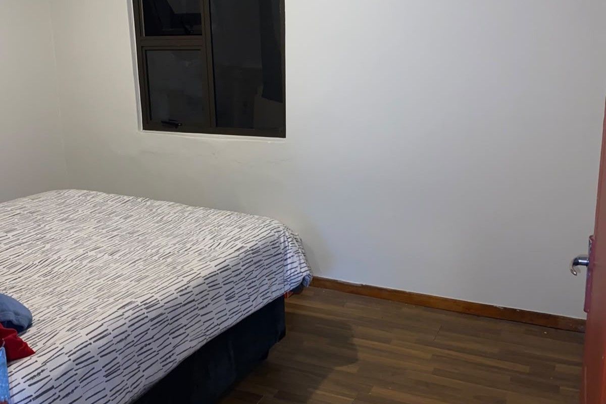 A simple bedroom featuring laminate flooring and an aluminium window frame, providing a neutral base for interior design.