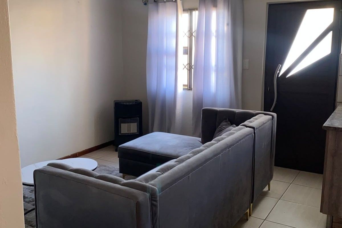 A compact living area featuring tiled flooring, a window with natural light, and a secure entrance door.