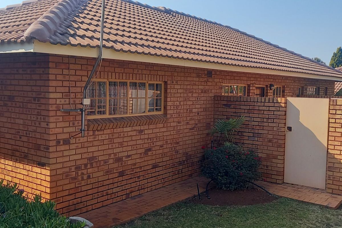A view of the rear exterior of the retirement village unit, featuring face brick construction, a tiled roof, and a private paved courtyard area.