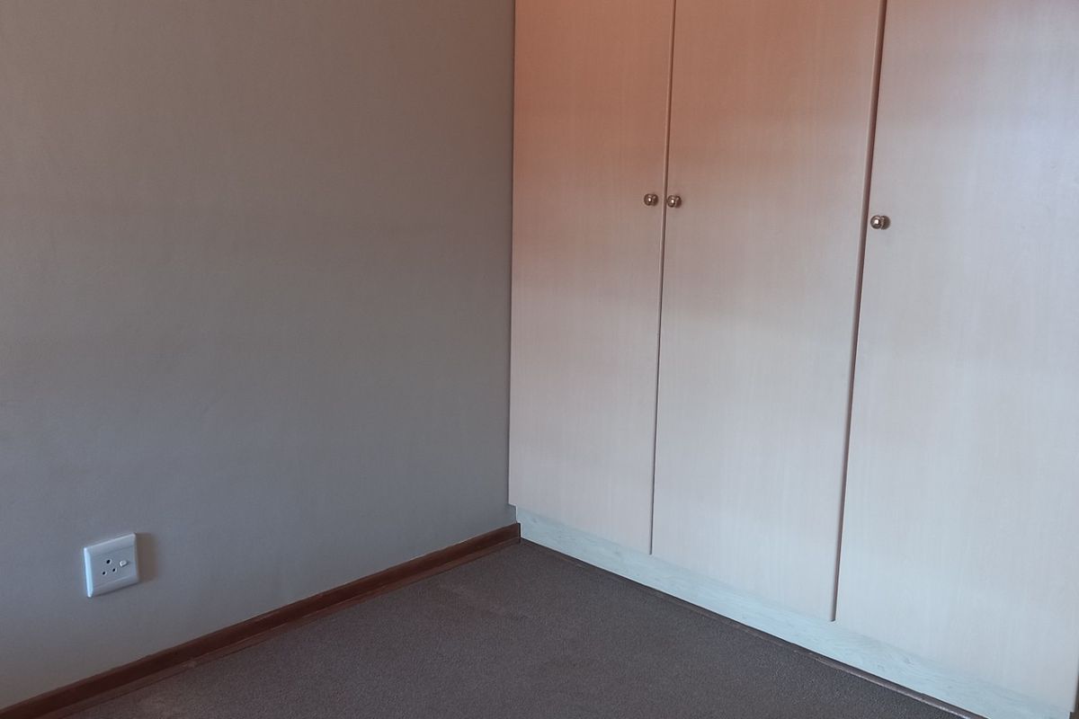 A clean, empty bedroom featuring neutral walls, carpeted flooring, and a functional built-in wardrobe with light wood-finish doors.