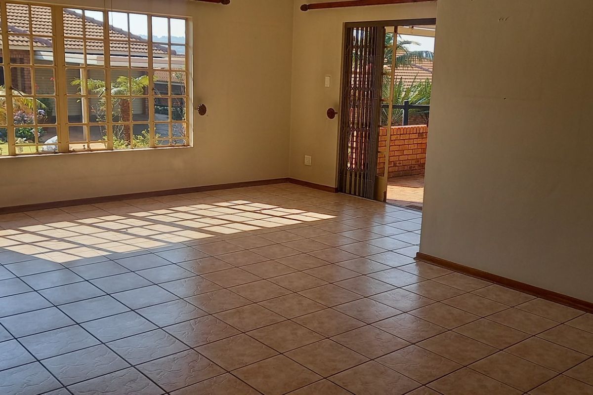 A spacious, sunlit living area featuring neutral tiled flooring, large windows, and direct access to an outdoor patio space.