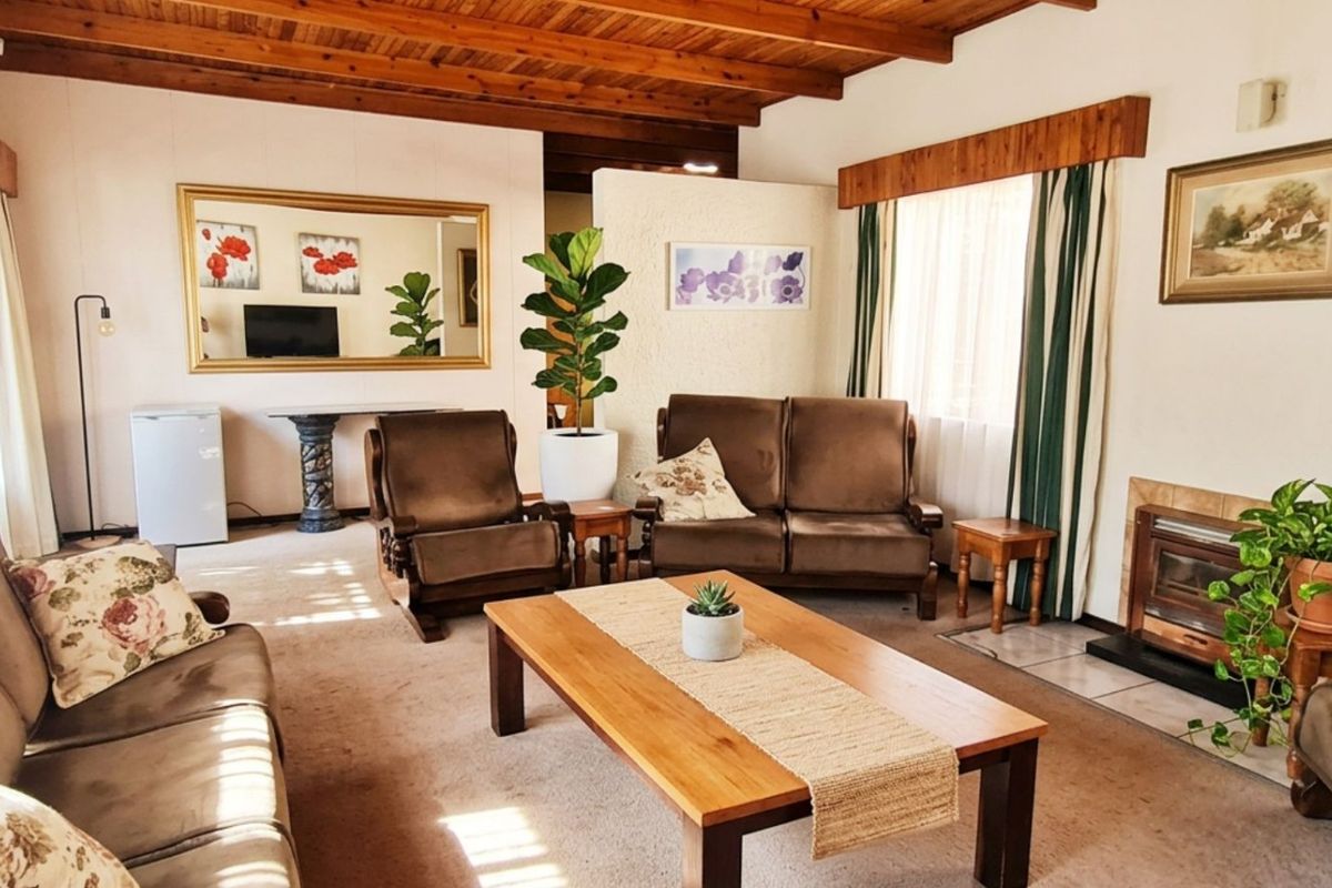 A cozy living room featuring a warm exposed timber beam ceiling and a traditional built-in fireplace with a tiled hearth.