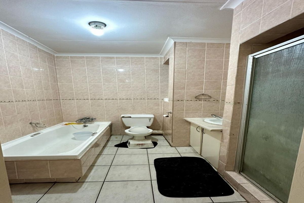 A dated bathroom featuring a built-in bathtub, separate shower enclosure, toilet, and vanity unit with tiled walls and flooring.