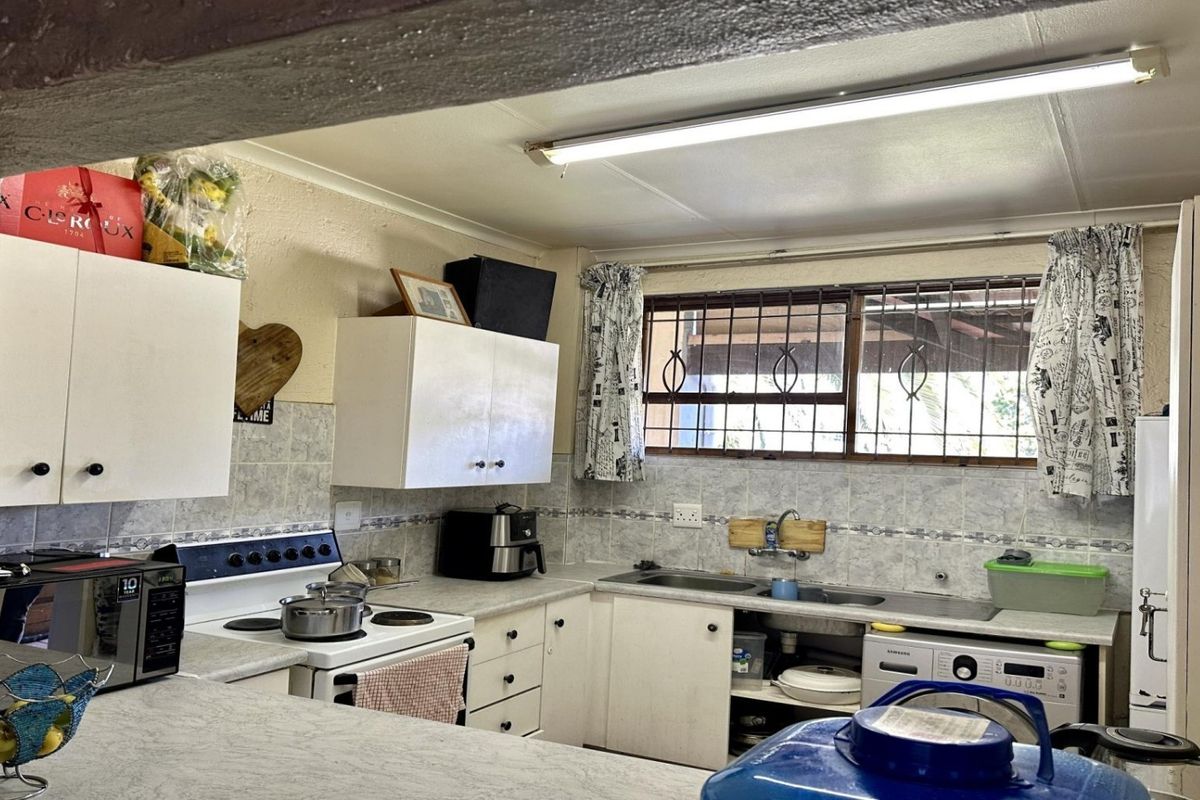 A functional kitchen featuring built-in cabinetry, laminate countertops, a double sink, and an electric stove, with security bars installed on the window.