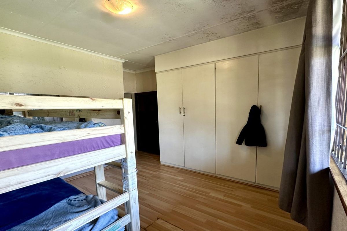 Bedroom featuring laminate flooring, built-in cupboards, and security bars on the window. The ceiling shows visible signs of water damage.
