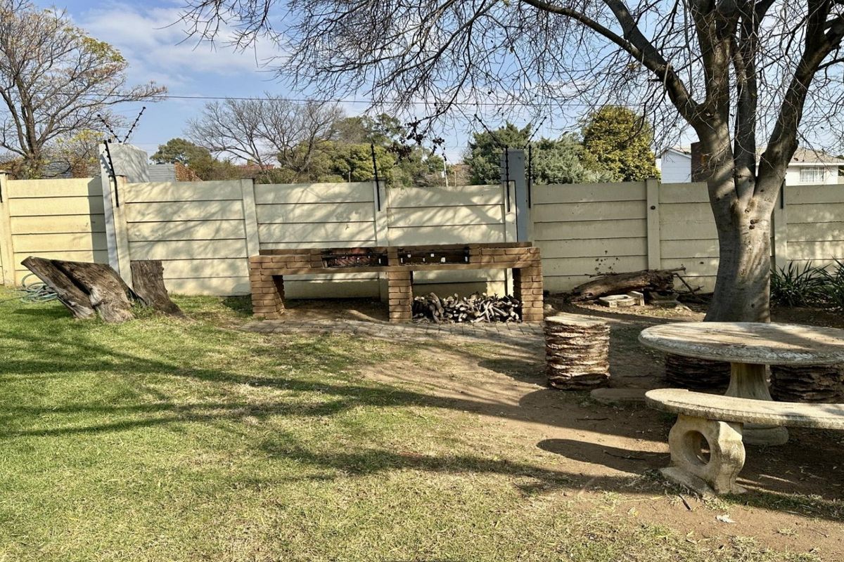 A private rear garden featuring a built-in brick braai, concrete seating, and secure boundary walling with electric fencing.