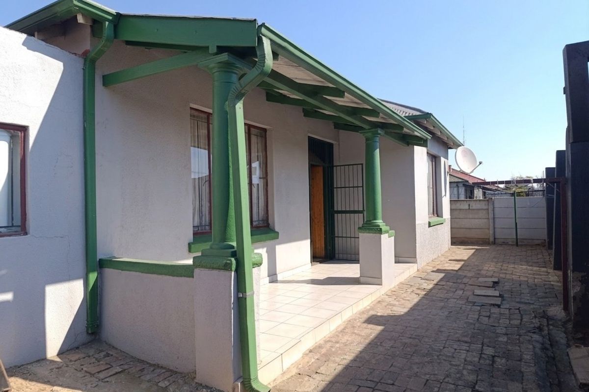 A rear exterior view of the house featuring a covered tiled patio with decorative columns, paved walkway, and functional guttering system.