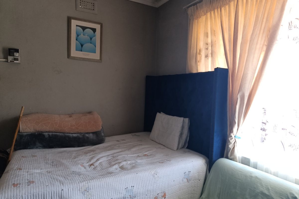 A bedroom featuring a window with curtains and wall-mounted ventilation, requiring cosmetic updates to the wall finishes.