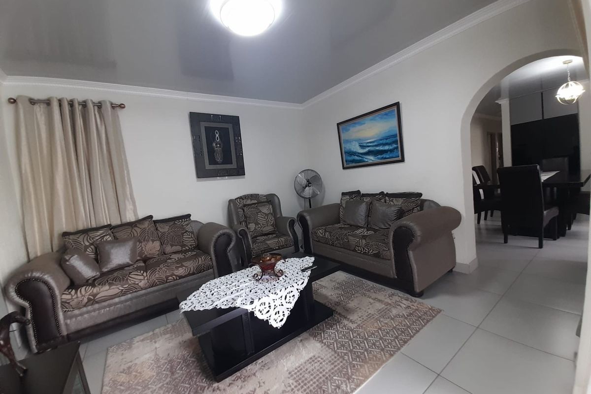 A well-maintained living room featuring glossy ceilings, tiled flooring, and an arched entryway leading to the dining area.