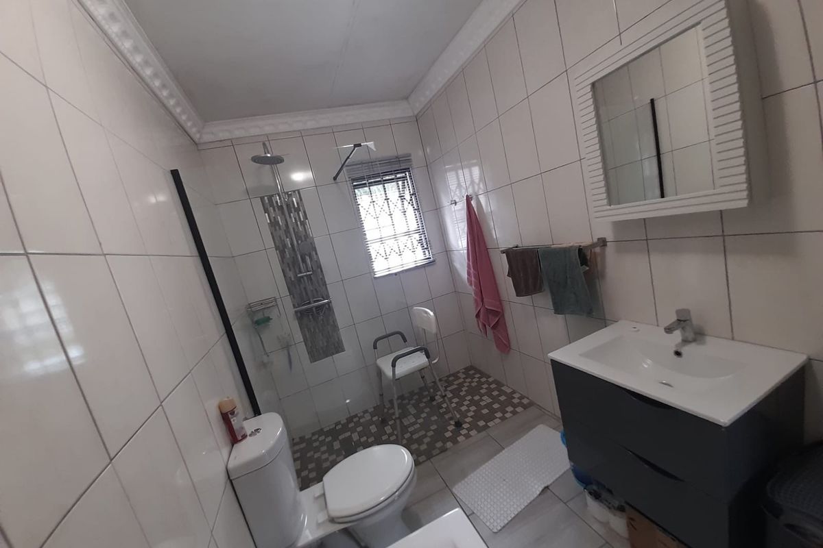 A functional bathroom featuring a walk-in shower, modern vanity unit with basin, toilet, and full-height wall tiling.