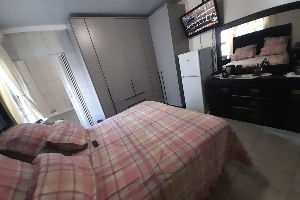 A bedroom featuring built-in wardrobes, tiled flooring, and coved ceiling details, offering a functional layout with direct access to an adjacent tiled area.