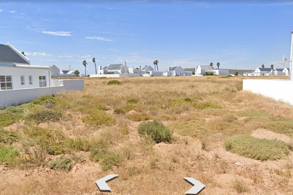A vacant residential plot situated between existing white-walled properties in a coastal estate setting.