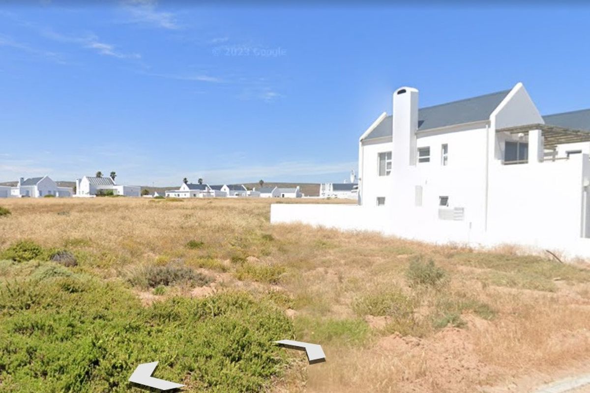 A vacant residential plot of land situated in a coastal estate, adjacent to existing white-walled residential properties.