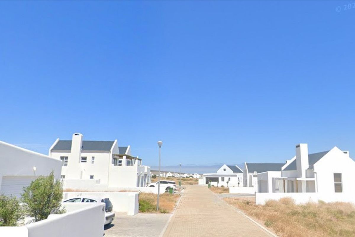 A street view of a residential neighborhood featuring paved driveways and modern white-walled homes under a clear blue sky.
