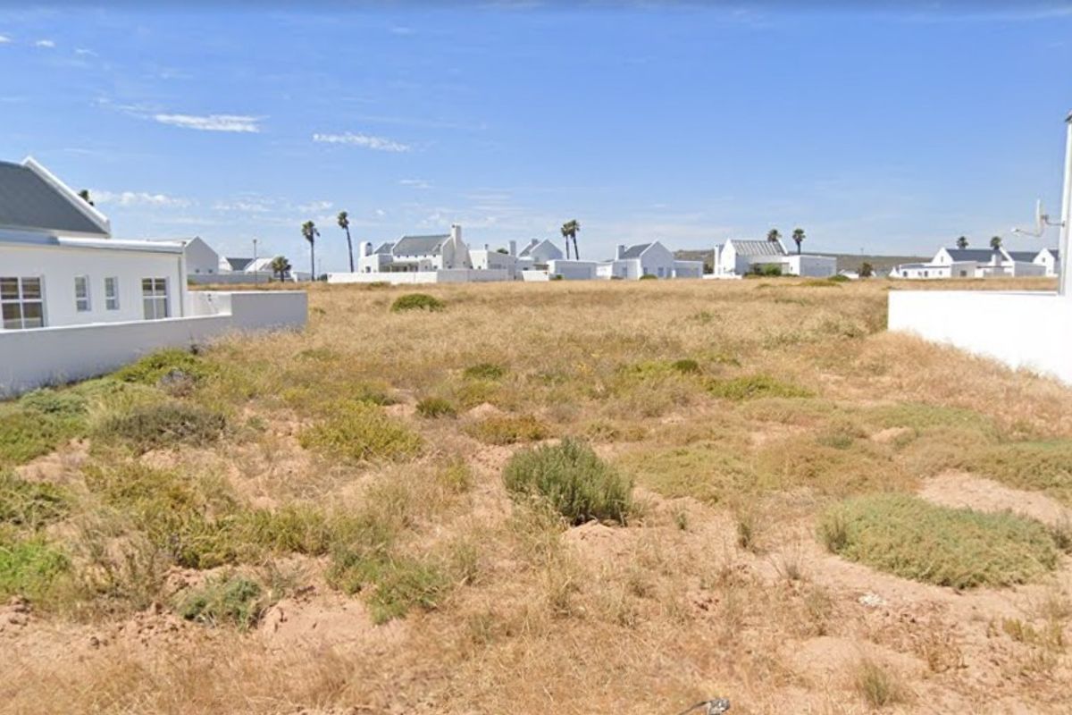 A vacant residential plot situated between existing white-walled properties, featuring natural ground cover and clear boundary lines.
