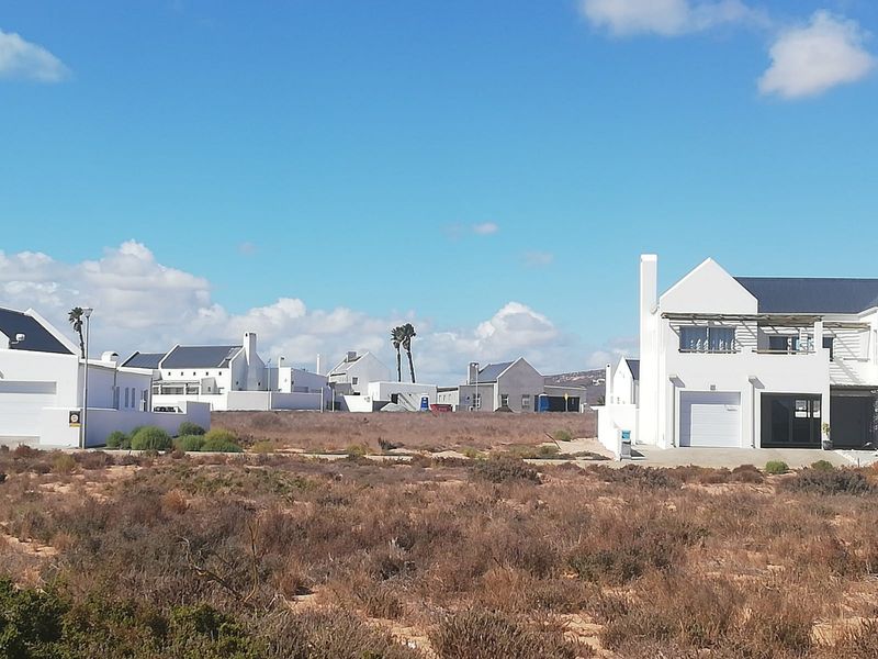 A view of a vacant residential plot situated within an established coastal estate, surrounded by modern white-walled homes.