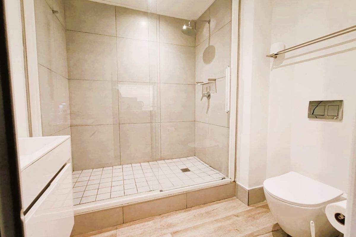 Modern bathroom featuring a walk-in shower with glass screen, wall-mounted toilet with concealed cistern, and vanity cabinet with wood-look flooring.
