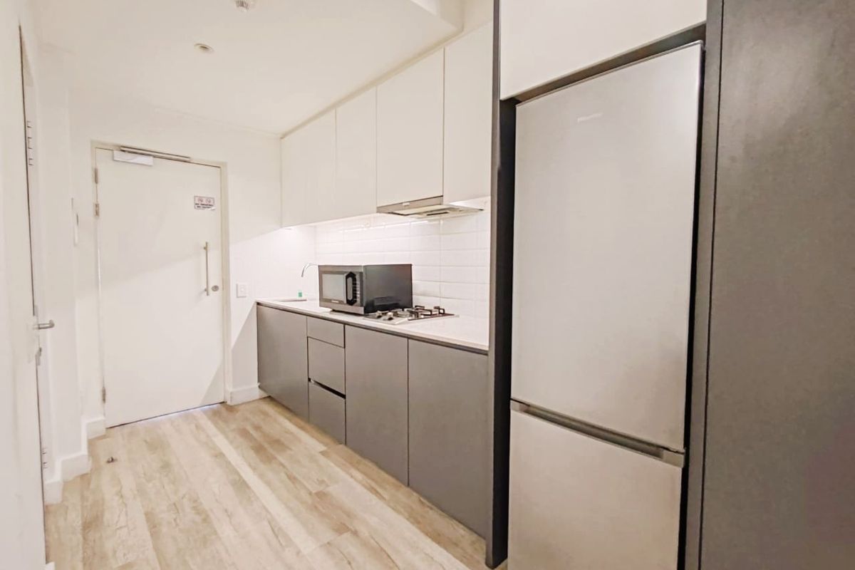 Modern galley-style kitchen featuring sleek two-tone cabinetry, a gas hob with extractor fan, subway tile backsplash, and light wood-look laminate flooring.