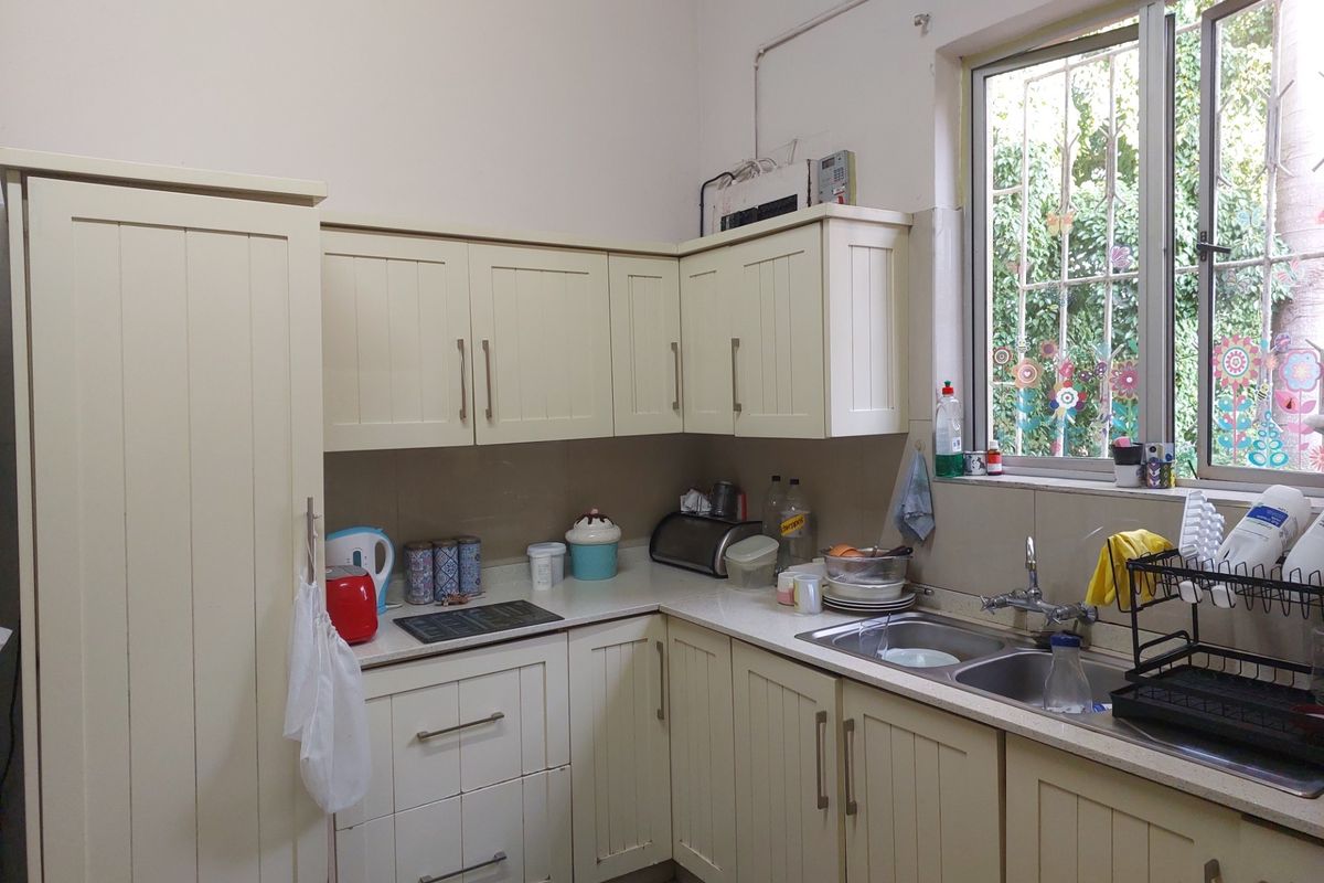 A functional kitchen featuring cream-colored cabinetry, laminate countertops, and a double bowl sink with a window providing natural light and garden views.