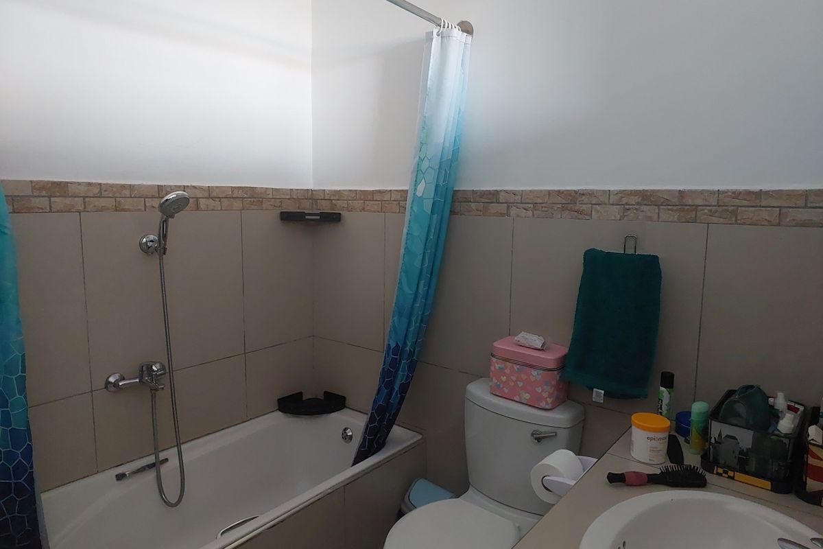 A functional bathroom featuring a bathtub with shower mixer, a toilet, and a vanity basin with tiled wall accents.