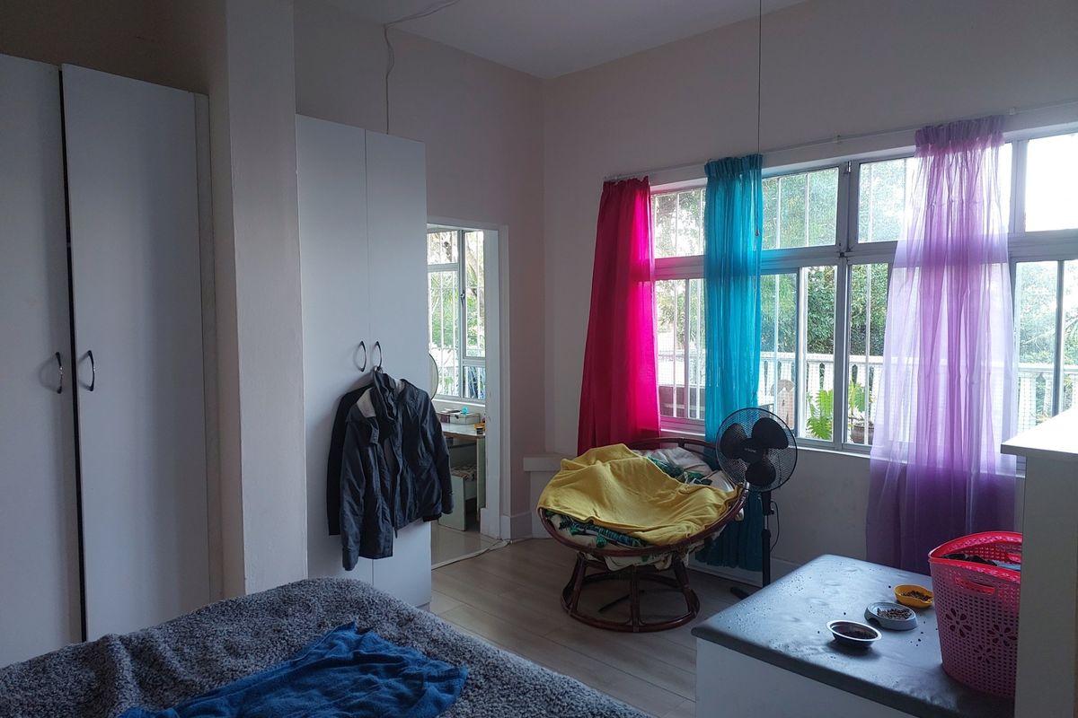 A bedroom featuring built-in wardrobes, laminate flooring, and large windows with security bars, offering natural light and access to an adjacent space.