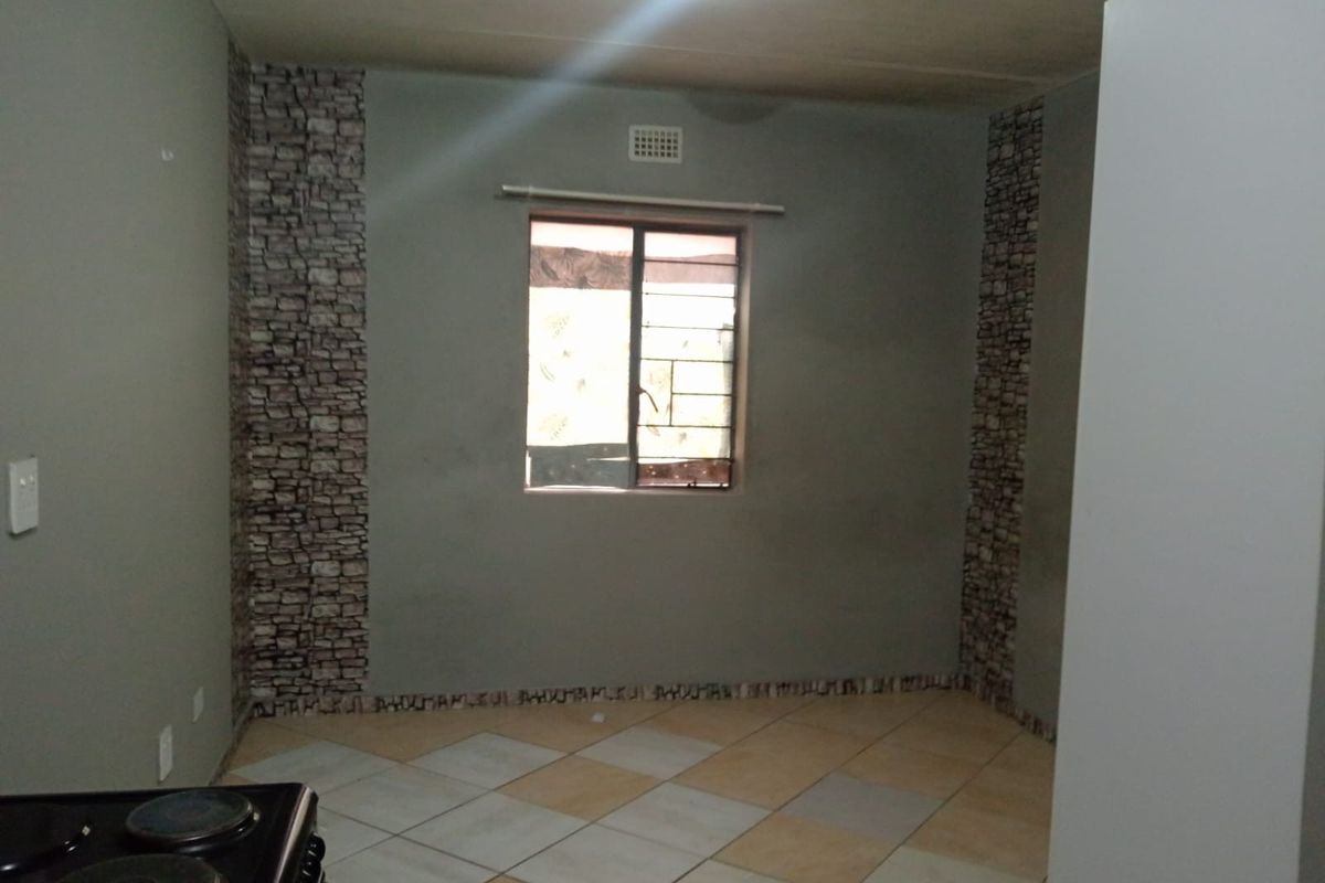 An empty kitchen area featuring tiled flooring, security bars on the window, and decorative stone-effect wall accents.