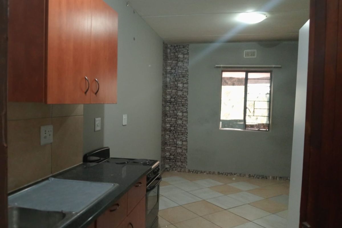 A functional kitchen space featuring built-in cabinetry, a stainless steel sink, and a freestanding stove, with tiled flooring and a window providing natural light.
