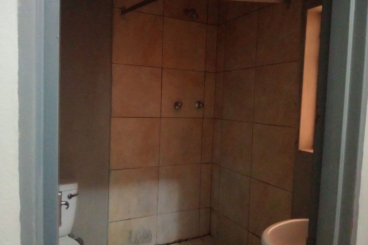 A compact bathroom featuring a tiled shower enclosure, pedestal basin, and toilet. The space requires cosmetic updates to improve its overall condition.