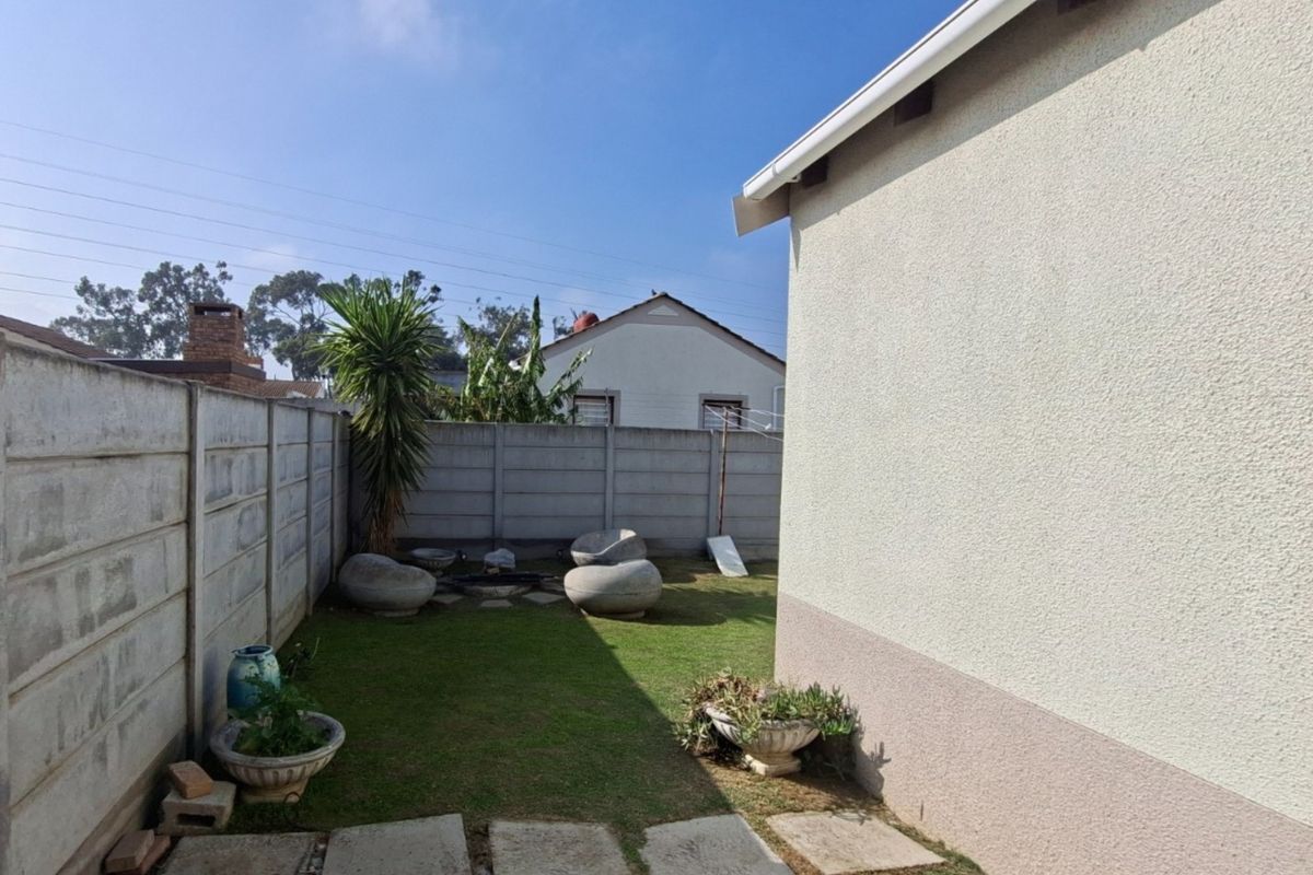 A view of the rear garden area featuring a lawn, paved walkway, and precast concrete boundary wall.