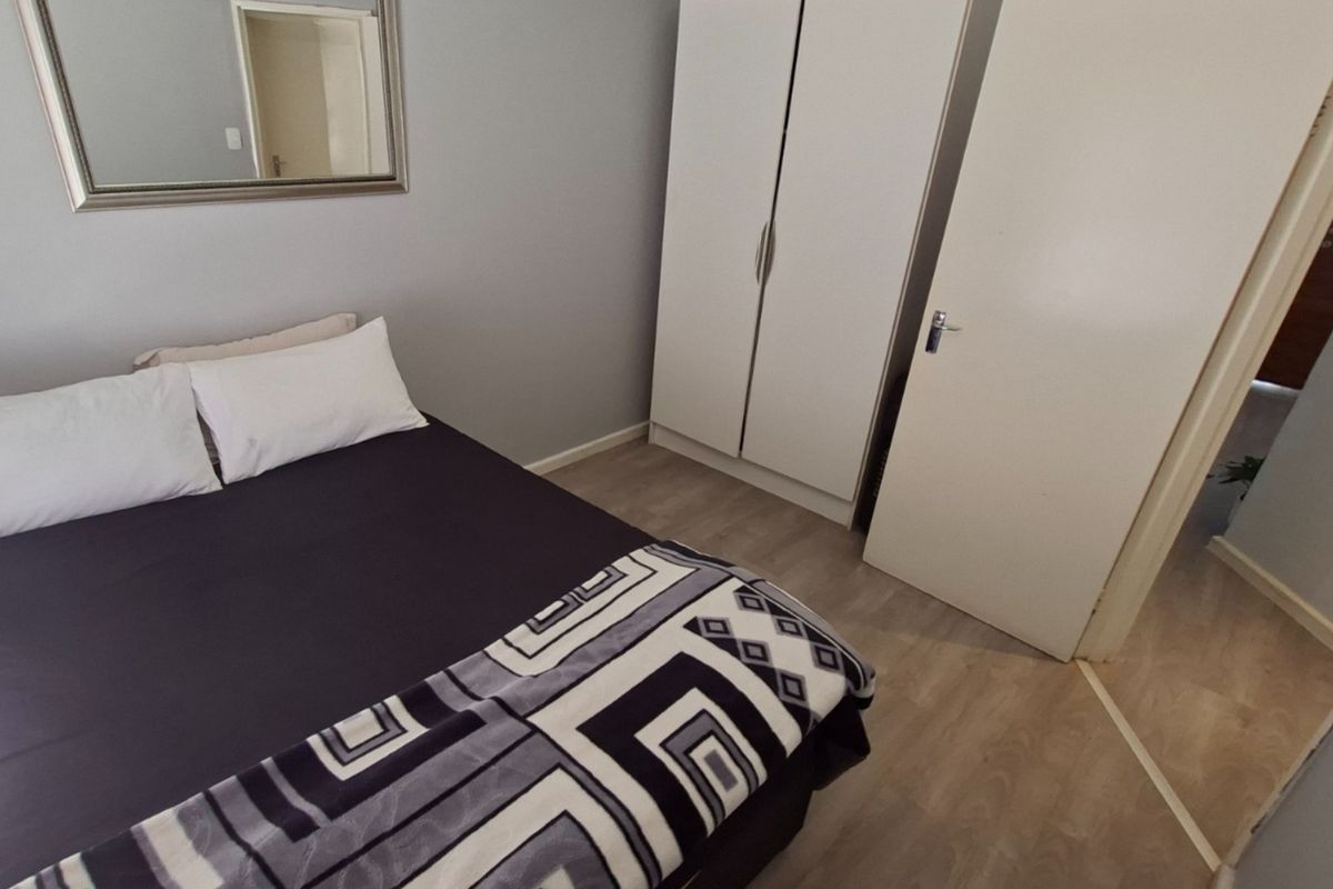 A well-maintained bedroom featuring light-toned laminate flooring and a functional built-in wardrobe.